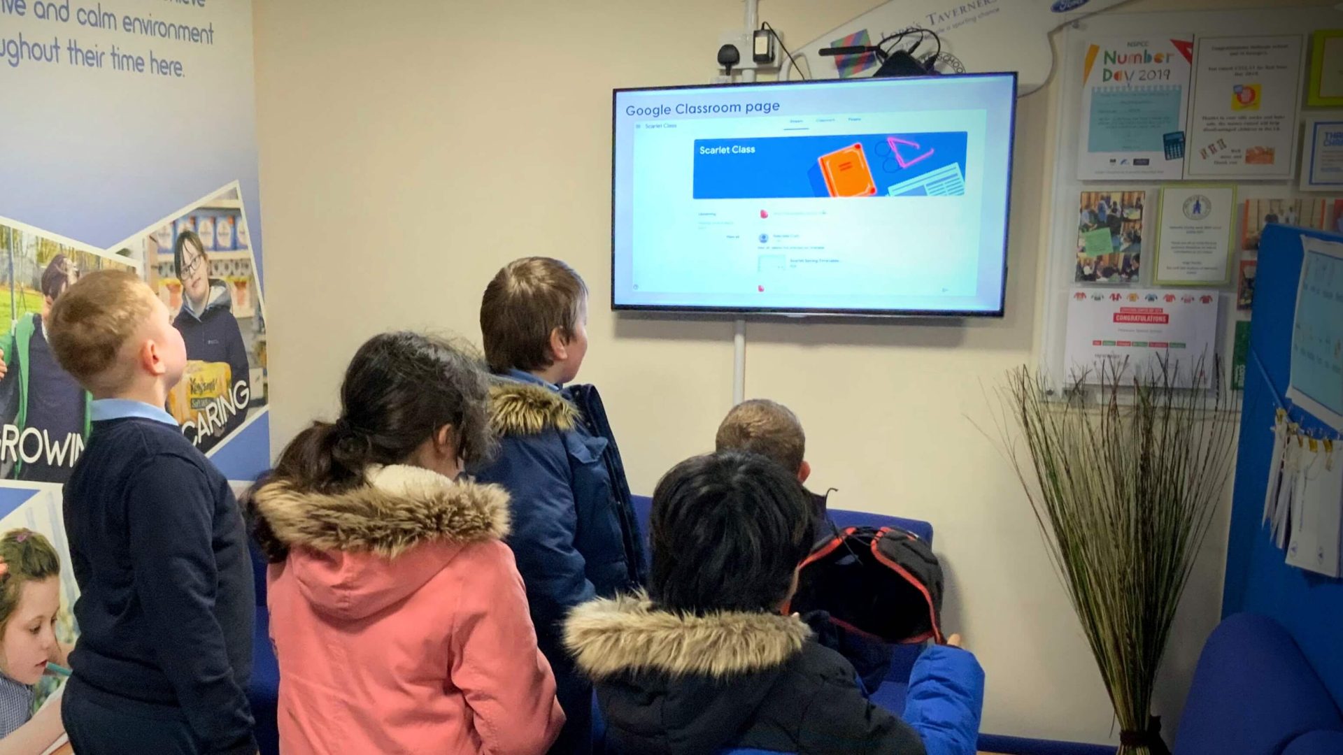 A picture of children looking at a digital signage screen running Google Classroom through TrilbyTV