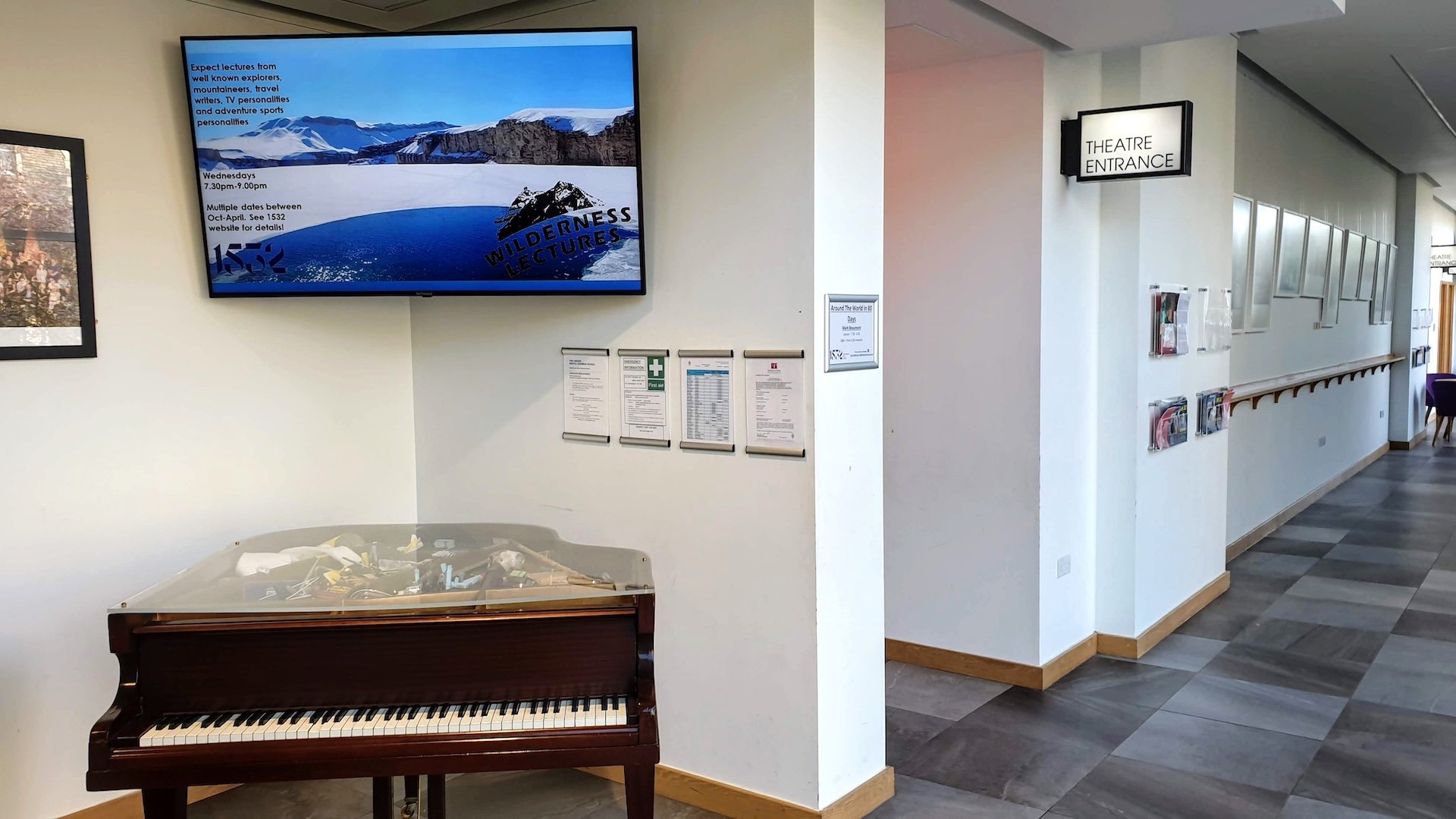 A digital signage screen at Bristol Grammar school displaying content via TrilbyTV in a corridor, by a piano and outside of the theatre entrance